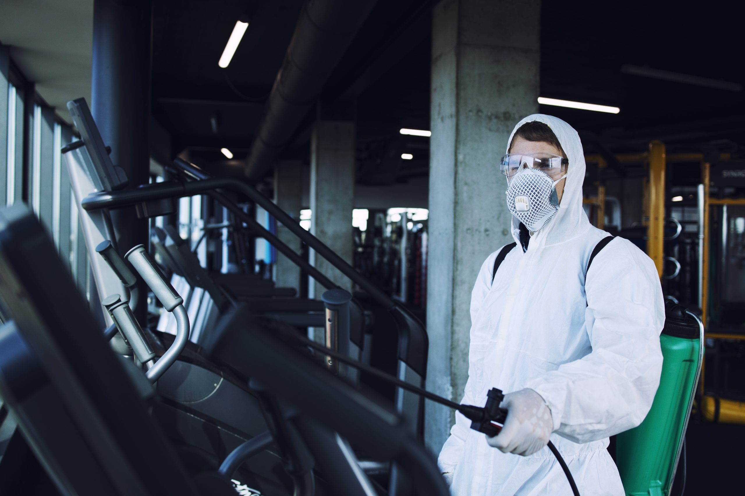 Técnico da Dourosafe com fato de proteção branco, máscara respiratória e pulverizador a realizar um serviço de desinfestação e controlo de pragas num ginásio.
